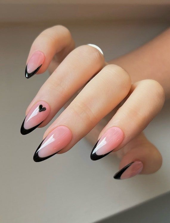 Almond-shaped nude pink nails with glossy black French tips and a small black heart accent, creating an elegant and modern manicure.