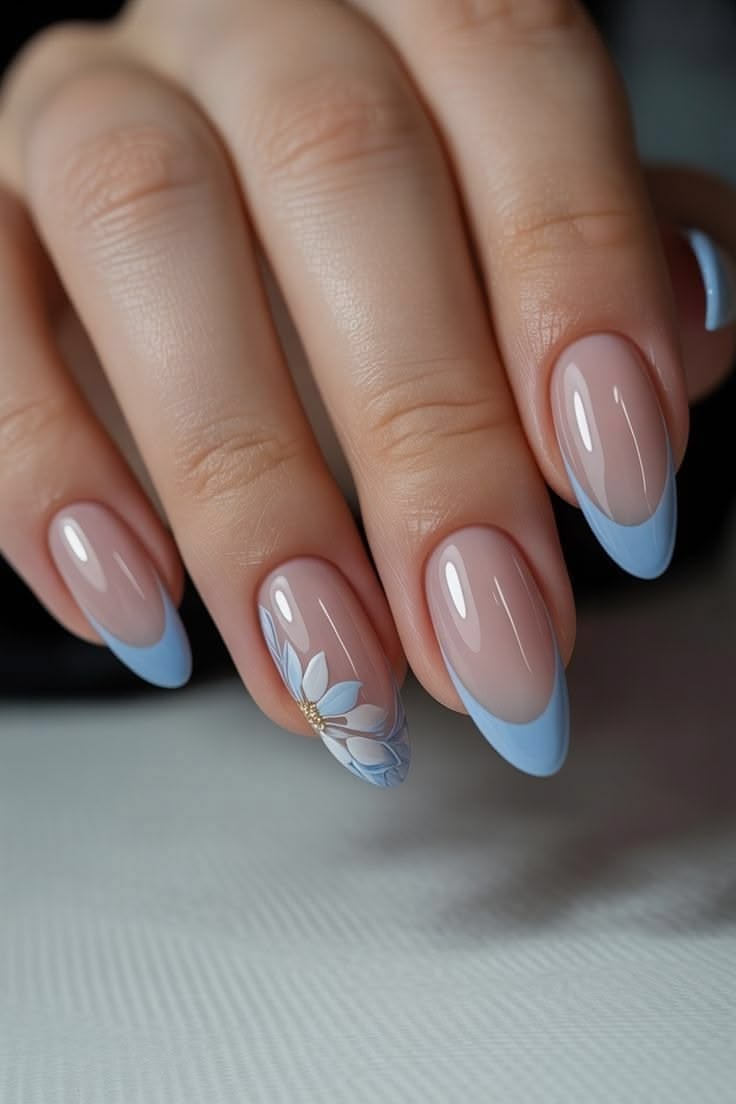 Medium-length almond-shaped nails with a high-gloss finish, featuring pastel cornflower blue French tips paired with a single accent nail on the ring finger decorated with a hand-painted blue and white daisy and a small textured gold center.