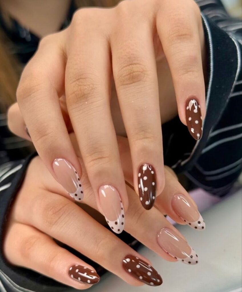 Medium-length almond-shaped nails with a high-gloss finish, featuring an alternating pattern of solid chocolate brown nails with white polka dots, and nude nails with off-white French tips decorated with small brown polka dots.