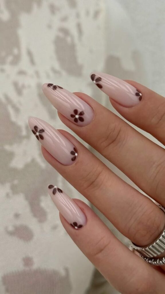 Long almond-shaped nails featuring a high-gloss semi-sheer milky pink base coat, decorated with hand-painted deep chocolate brown retro daisies with crisp white centers placed across the middle and edges of each nail.