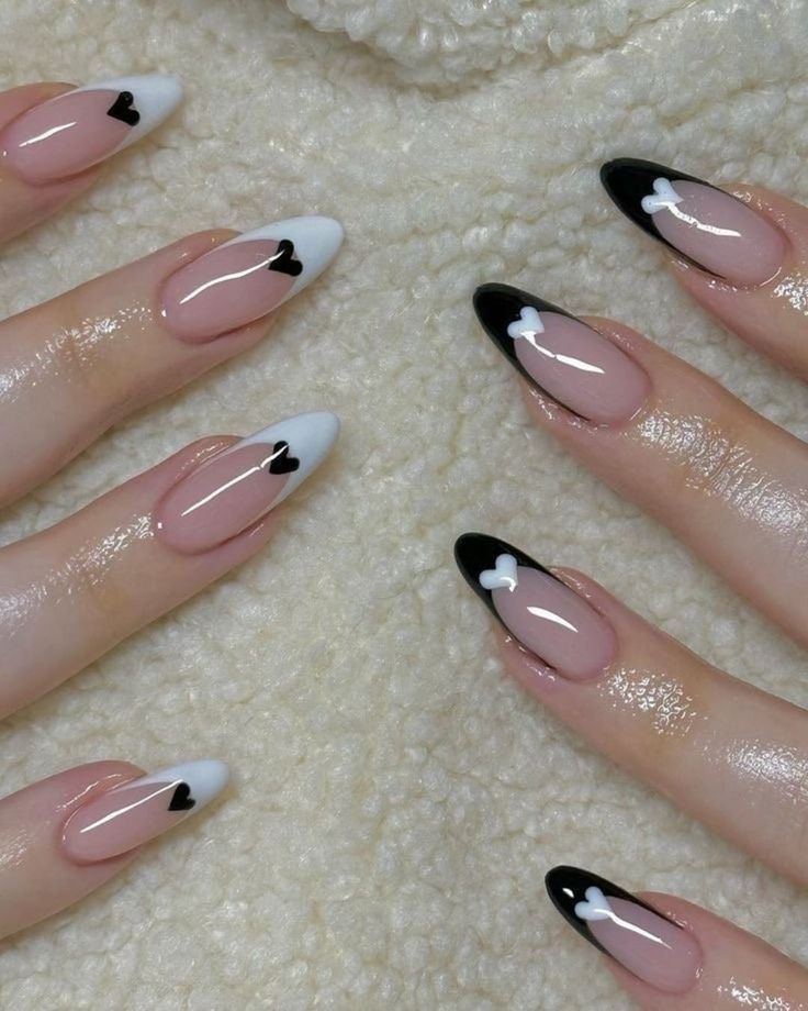 Medium-length almond-shaped nails with a high-gloss sheer pink base, featuring a mismatched French manicure where one hand has white tips with tiny black hearts and the other hand has black tips with tiny white hearts.