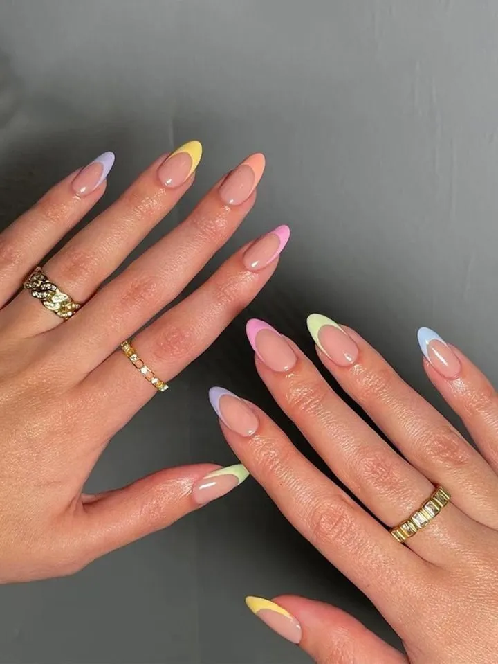Medium-length almond-shaped nails featuring a high-gloss natural pink base coat and a skittle-style French manicure, with each tip painted in a different creamy pastel color, including pink, purple, yellow, green, orange, and blue.