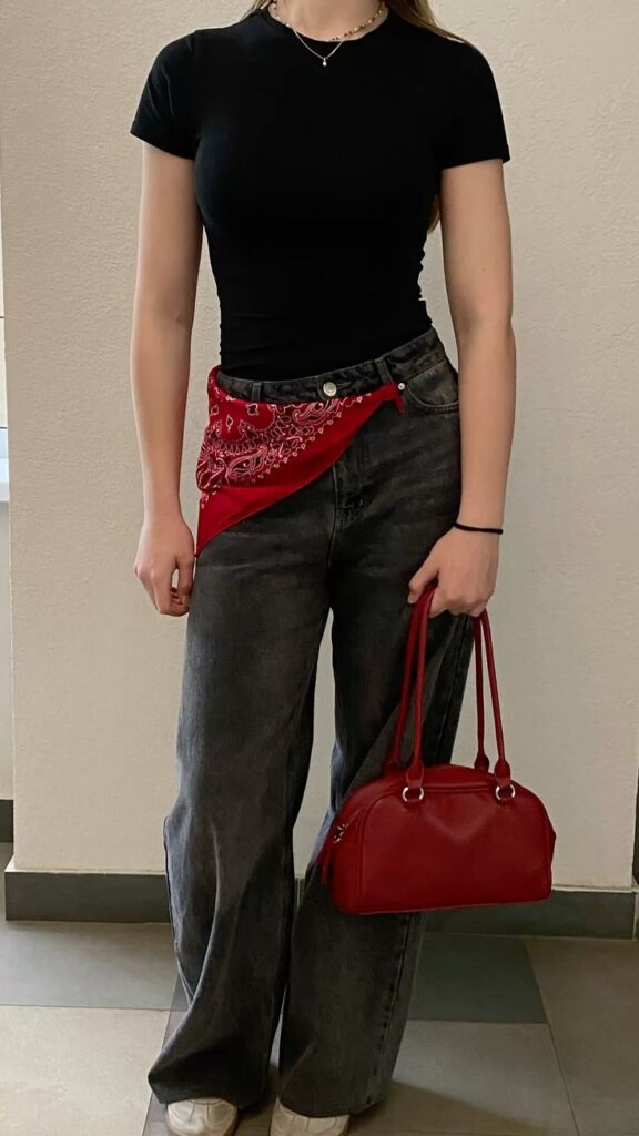 A woman showcasing how to style a bandana or scarf as a belt. A red paisley bandana is tied through the loops of her grey jeans.
