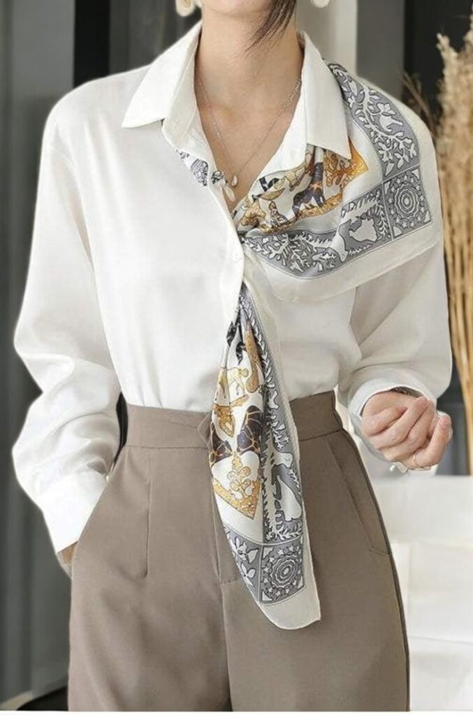 Close up of a woman showing how to style a bandana or scarf with a white button-down shirt. A patterned silk scarf is draped elegantly under her collar.