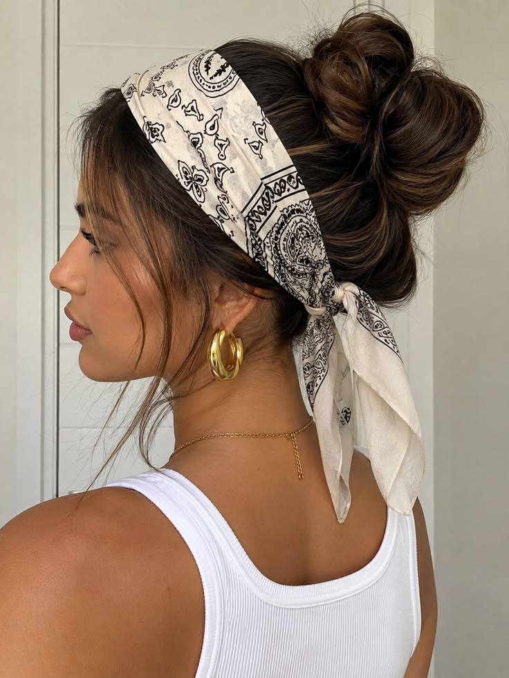 Side profile of a woman showing how to style a bandana or scarf. A white paisley bandana is wrapped around her head with a large messy bun.