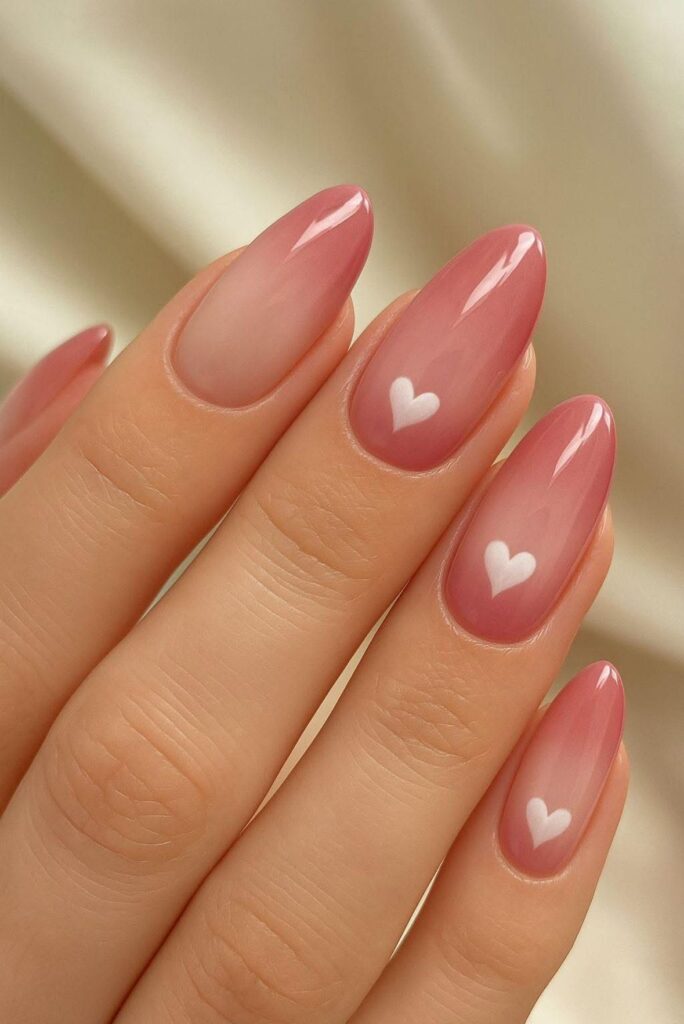 Glossy almond-shaped nails with a sheer jelly pink base coat, featuring a small, soft white heart painted in the center of the middle, ring, and pinky nails.