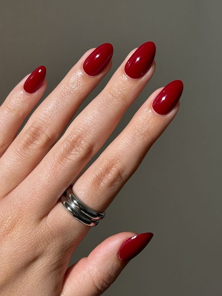 Timeless cherry red nails, glossy medium almond manicure, and bold solid red cream minimalist nail design with silver ring jewelry.