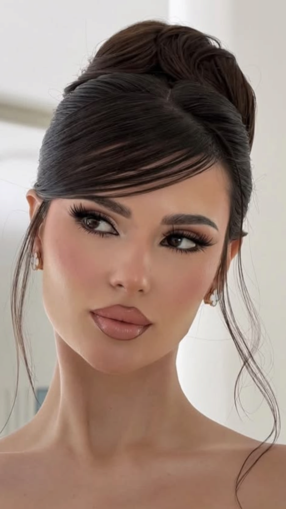A beautiful woman with an elegant 90s high bun hairstyle, featuring side-swept bangs and loose hair pieces framing her face.