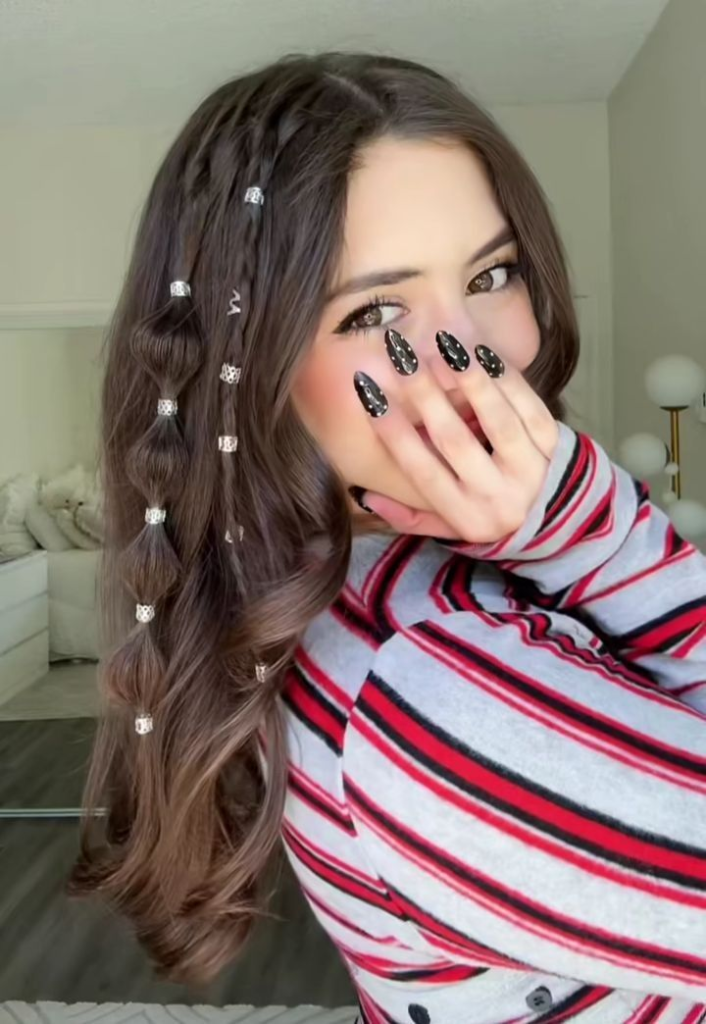 A young woman with long brown hair featuring a side bubble braid and a small accent braid, both decorated with silver metallic hair cuffs.
