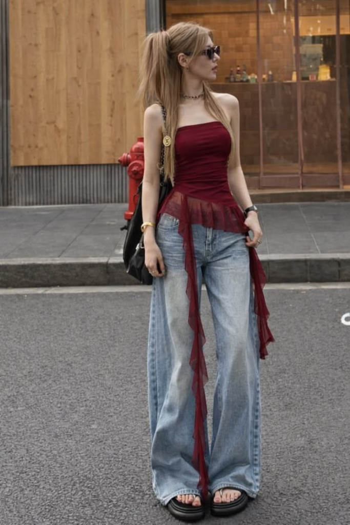 A girl wearing a red strapless top with mesh detail, loose blue jeans, and black sandals.