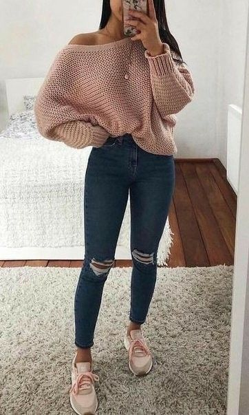 A girl taking a mirror selfie wearing an oversized pink knit sweater, dark blue ripped skinny jeans, and pink sneakers.