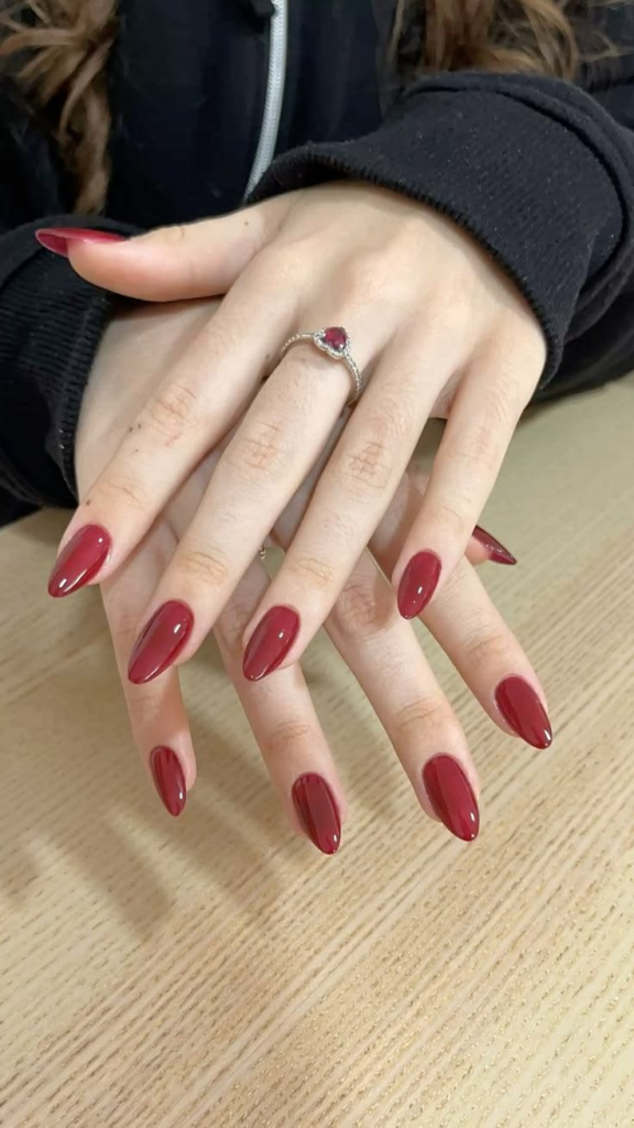 Classic cranberry red nails, glossy medium almond manicure, and elegant solid red cream minimalist nail design.