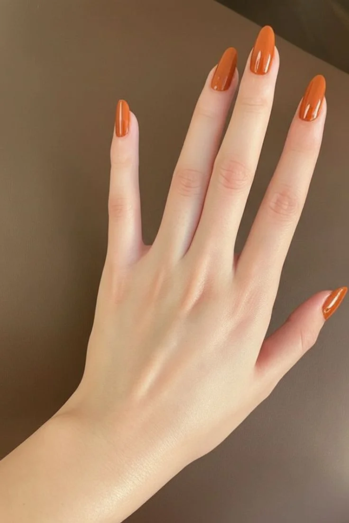 Rich terracotta orange nails, solid burnt orange cream manicure on long almond nails, and minimalist everyday warm autumn nail design.
