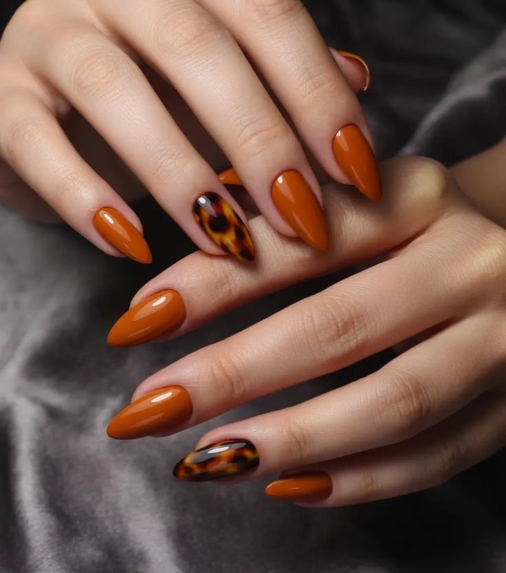 Terracotta orange fall nails with tortoiseshell accent nails, glossy almond-shaped autumn manicure, and trendy pumpkin spice nail art.