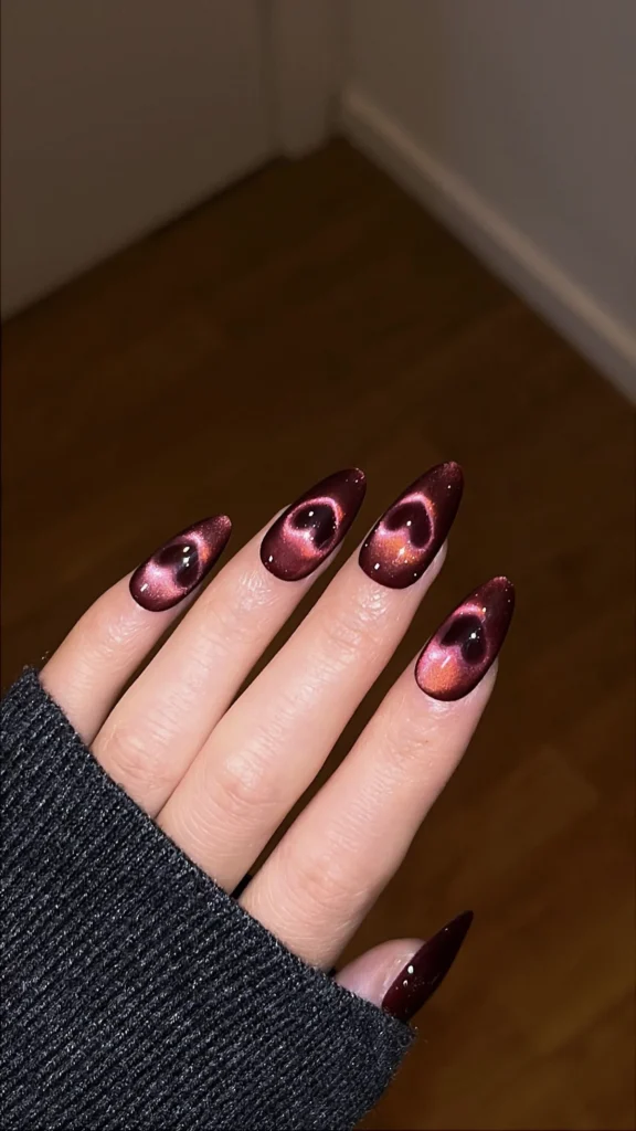 Long, almond-shaped nails featuring a dark burgundy base with mesmerizing 3D glowing rose-gold magnetic heart cat eye nail designs.