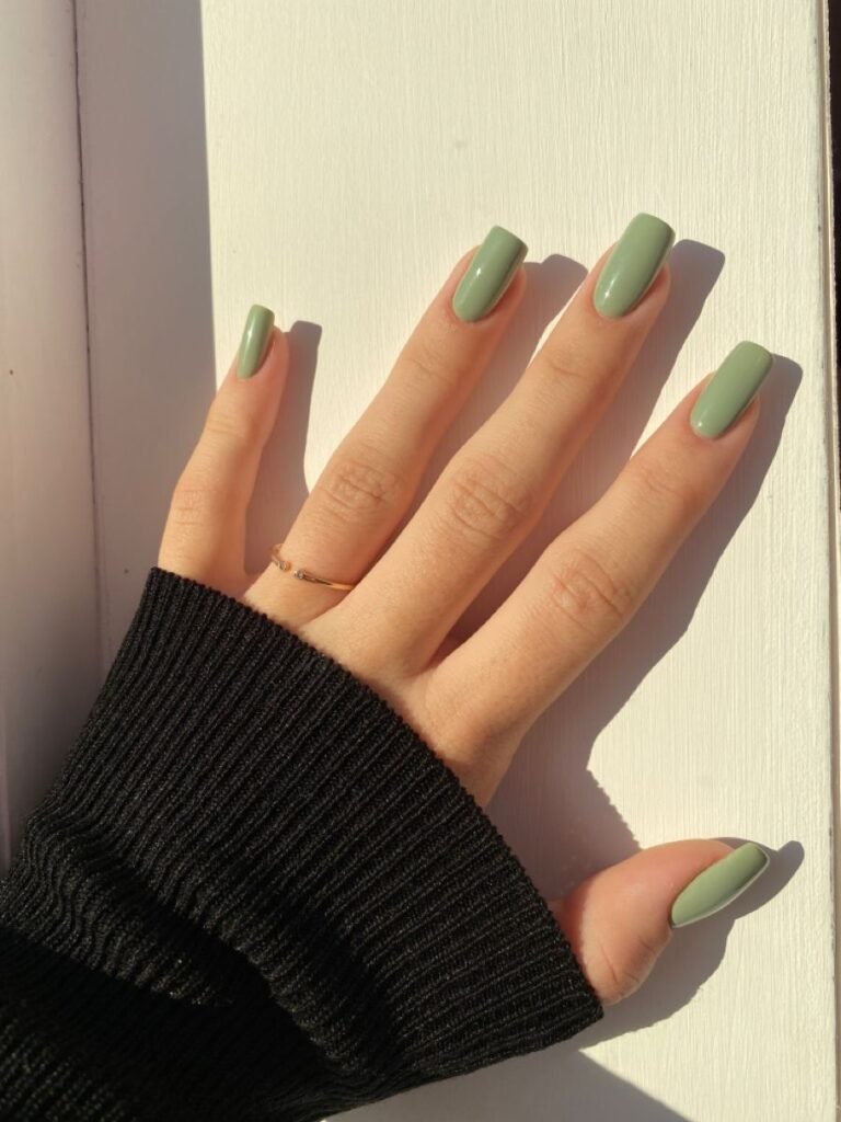 Glossy sage green square-shaped nails with a minimalist solid color manicure in natural sunlight.