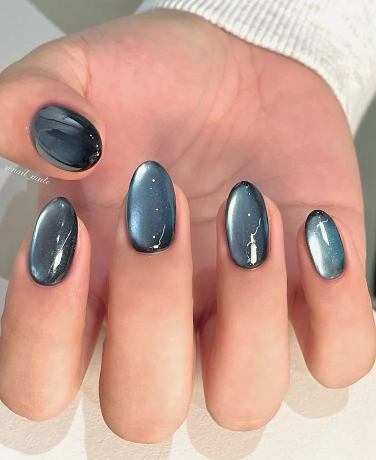 Oval-shaped nails featuring a sleek steel-blue and silver velvet magnetic cat eye nail designs effect over a dark base.