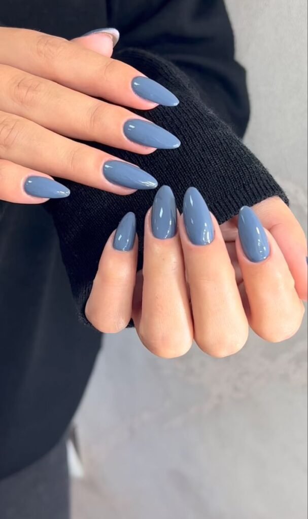Glossy slate blue almond-shaped nails with a minimalist solid color manicure and cozy black sweater.