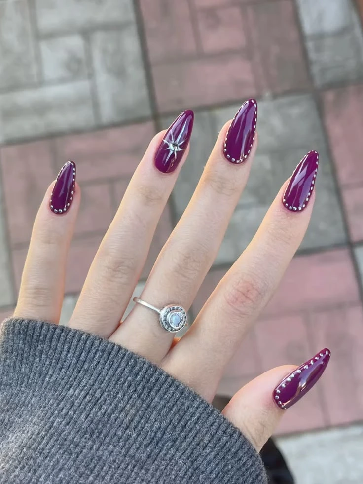 Luxury royal plum almond nails with silver studded borders, celestial starburst nail art, and sparkling gemstone accents