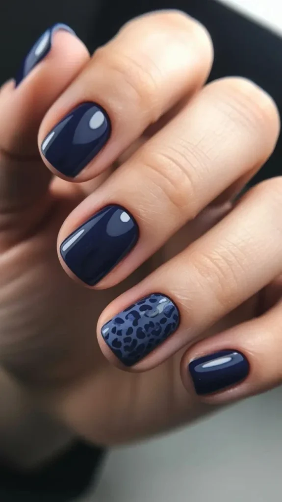 A close-up beauty shot of short nail ideas featuring a glossy deep navy manicure on short squoval nails with a dark blue leopard print accent nail.