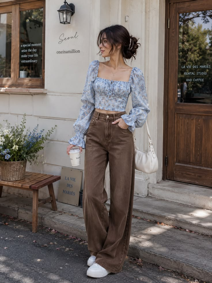 Woman wearing a blue floral crop top with brown wide-leg pants, white sneakers, and a white shoulder bag.