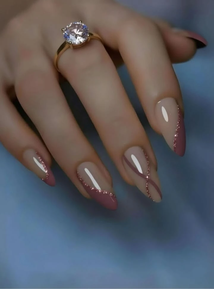 A close-up luxury beauty shot of trendy and luxurious nail ideas featuring sleek almond nails with a neutral base, rose mauve diagonal tips, and sparkling glitter swirl lines, styled with a diamond gold ring.