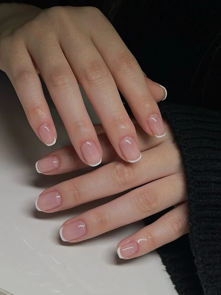 A close-up beauty shot of clean and minimalist nail ideas featuring short natural nails with a classic ultra-thin white micro-French tip design and a high-shine finish.