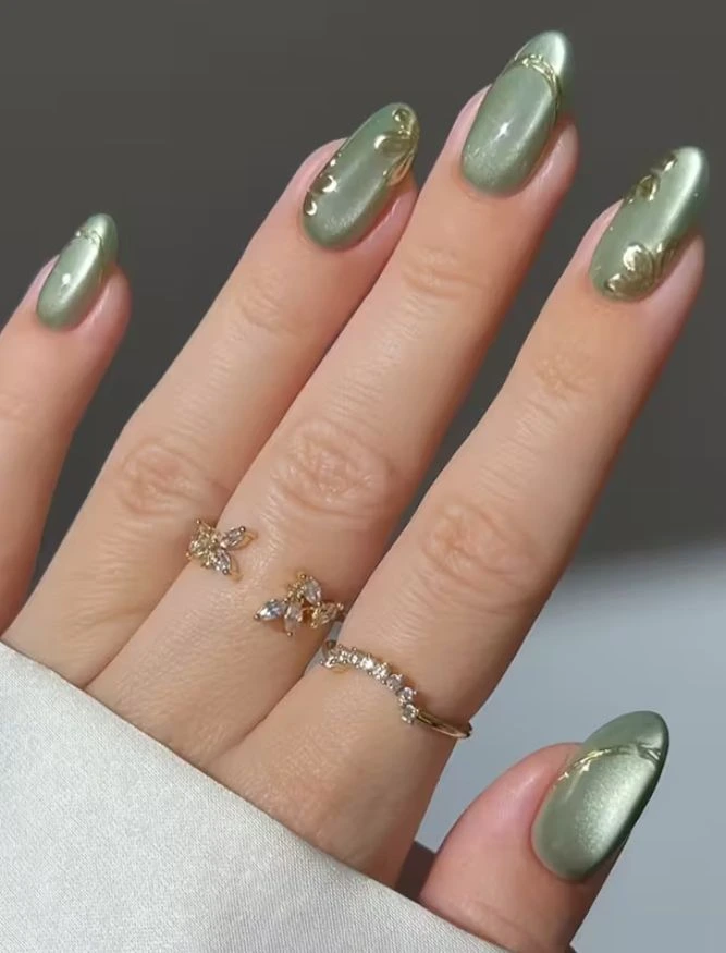 A close-up beauty shot of luxurious nail designs featuring almond-shaped cat-eye sage green nails with raised gold relief and vintage metallic details.