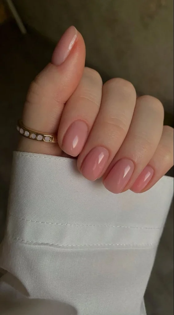 A close-up beauty shot of clean and minimalist nail ideas featuring short rounded nails with a warm glossy nude polish and high-shine finish.