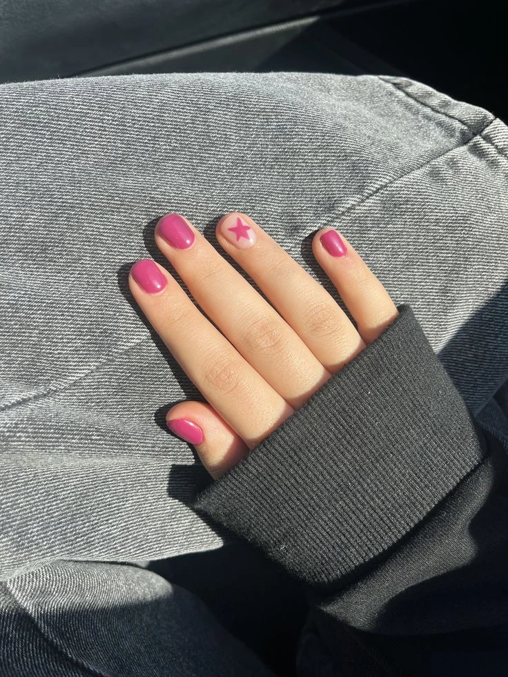 A close-up beauty shot of cute and playful short nail ideas featuring short rounded nails with glossy magenta polish and a sheer accent nail featuring a pink star design.