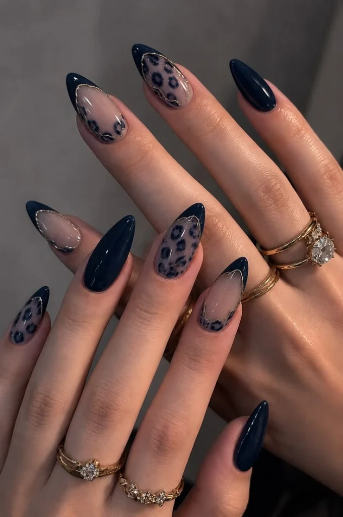 A close-up luxury beauty shot of trendy and luxurious nail designs featuring sleek almond nails with solid dark navy polish, sheer nude bases, metallic silver chrome outlines, and navy leopard print art, styled with gold rings.