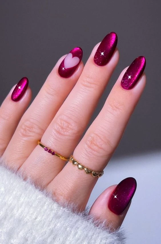 A close-up beauty shot of luxurious nail designs featuring almond-shaped magnetic berry cat-eye nails with a negative-space cut-out heart accent.